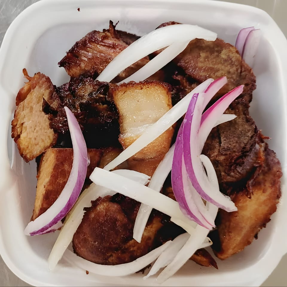 Fried pork (griot) with white and red onion slices in a white container from Vingoute Restaurant.
