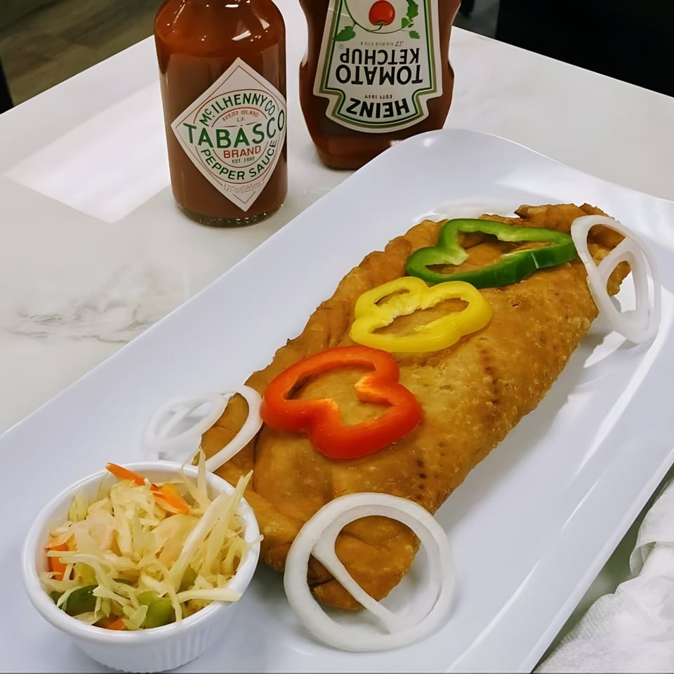 A golden-brown Haitian pate, topped with bell peppers and onions, served with pikliz and hot sauces.