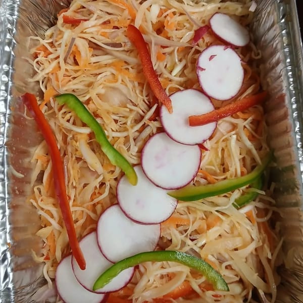Haitian pikliz in a foil container, with shredded cabbage, carrots, bell peppers, and radishes.
