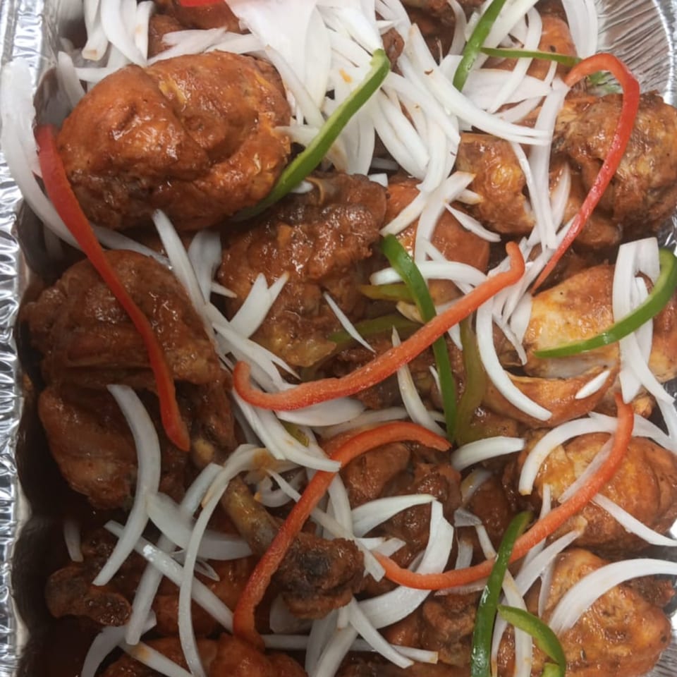 Haitian fried chicken with sliced white onions, red, and green bell peppers in a foil pan.