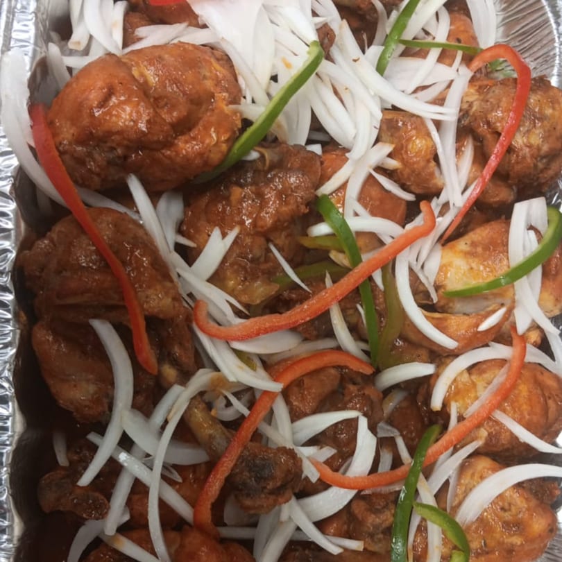 Haitian fried chicken with sliced white onions, red, and green bell peppers in a foil pan.