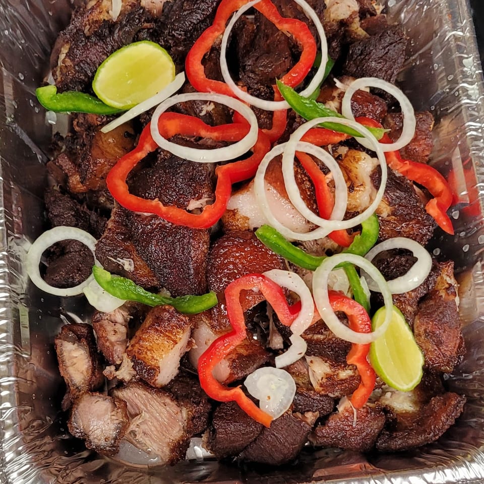 Haitian griot, fried pork pieces, garnished with red and green bell peppers, onions, and lime.
