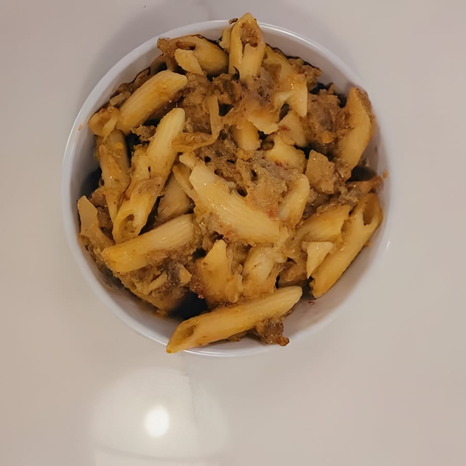 A white bowl filled with Haitian penne pasta and ground meat, viewed from above.