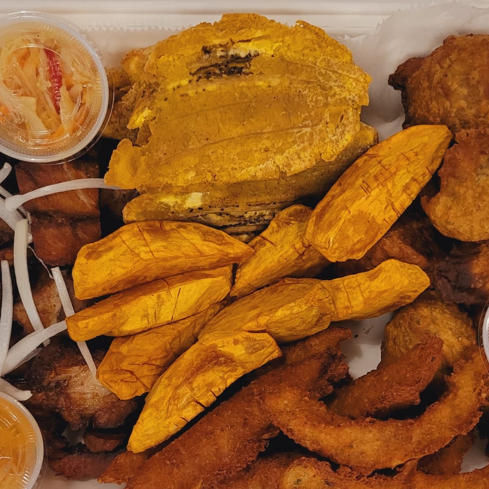 A close-up of a Haitian griot platter with fried plantains, pikliz, and other fried foods.