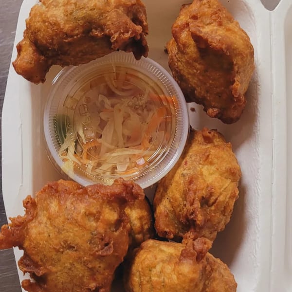 Golden-brown fried Haitian fritters and a small container of pickled vegetables in a white takeout box.