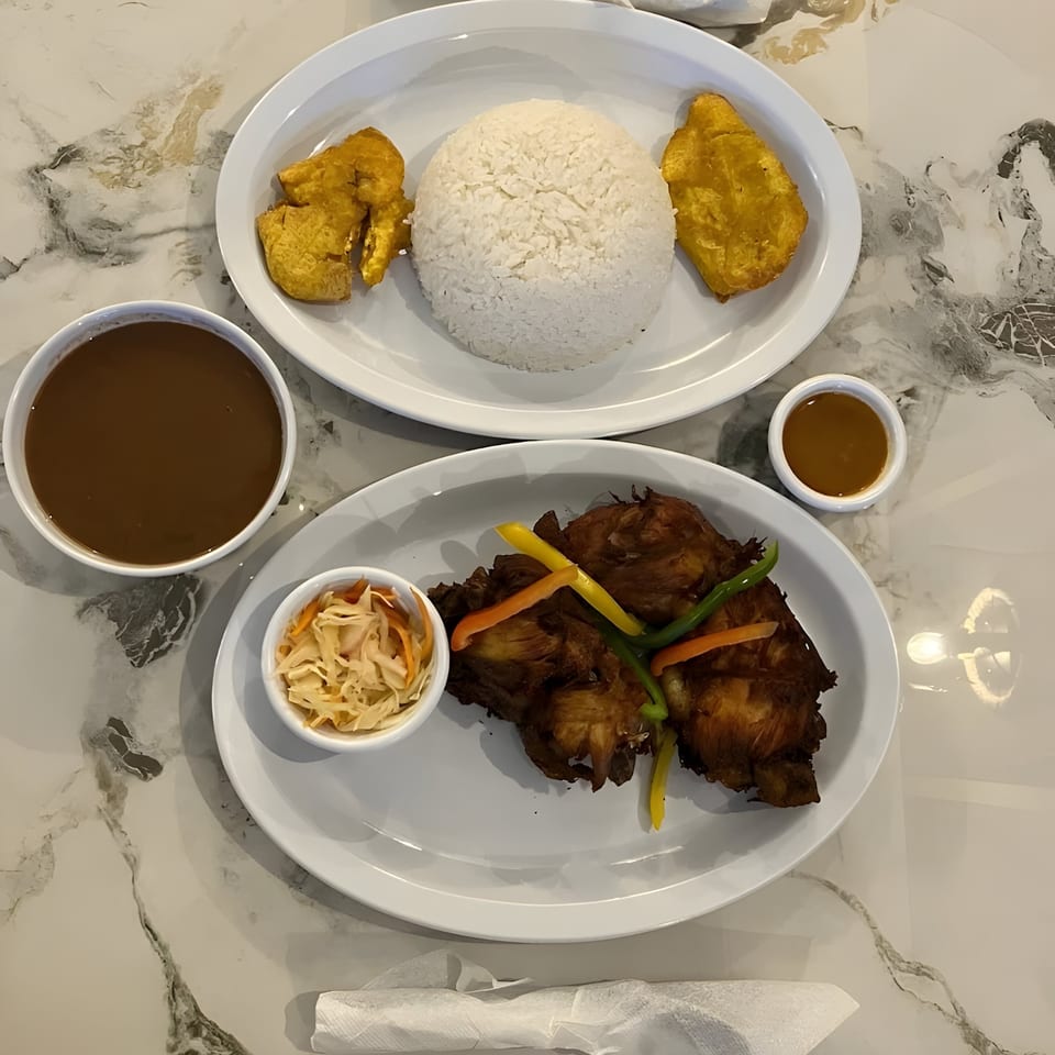 Haitian meal with fried chicken, rice, plantains, pikliz, and two bowls of sauce on a marble table.