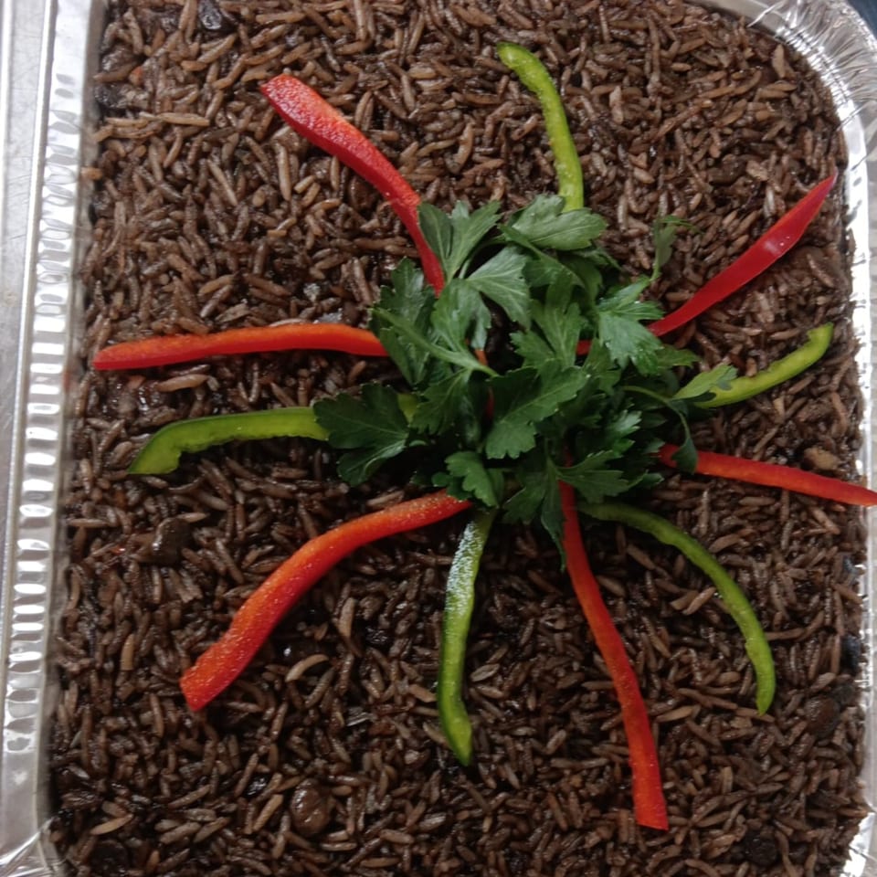 Haitian black rice (diri djondjon) in a foil pan, garnished with red and green bell pepper strips and parsley.
