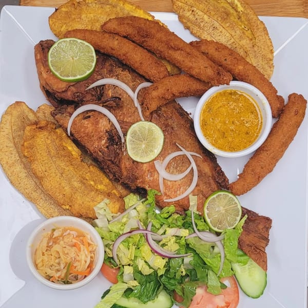 A Haitian fried fish platter with plantains, salad, and two dipping sauces on a white plate.