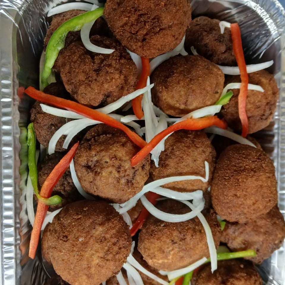Haitian fried meatballs with sliced white onions, red and green bell peppers in a foil container.